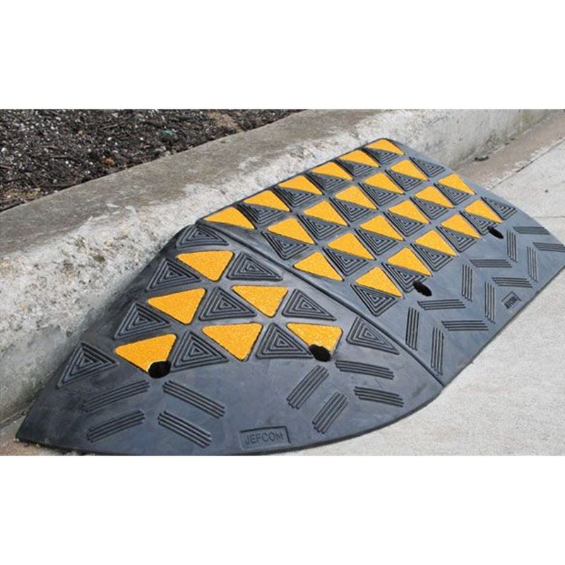 krr100 Hi-Viz Kerb Ramp Body Rubber - 610mm x 320mm x 100mm - Black/Yellow 2 Black and yellow rubber speed bump with triangular patterns on a concrete surface, used for traffic calming and pedestrian safety.