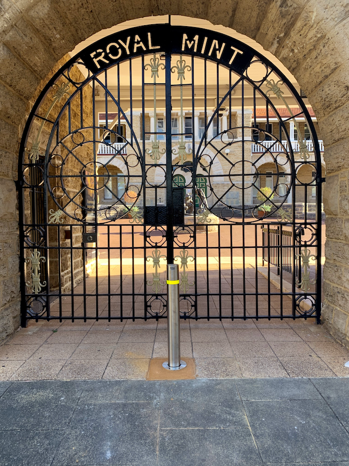 COMPANY PROFILE About Us 2 Ornate Royal Mint gate with filigree design, set in a stone archway. A silver bollard stands in front, enhancing security. About Us.
