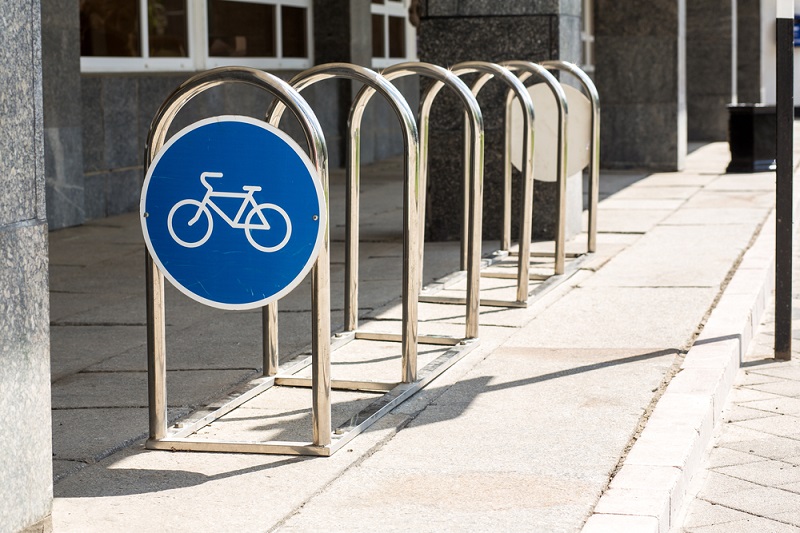 Bike racks for business use. Metal bike rack with blue sign showing bicycle symbol on a concrete sidewalk.