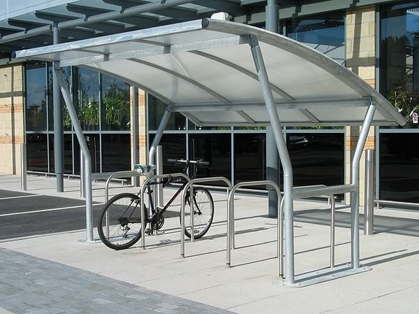 Bike Racks Five Reasons to Encourage Your Team to Bike to Work 1 Bike rack shelter for encouraging team to bike to work. Covered bicycle parking area with one bike parked. Workplace bike storage.
