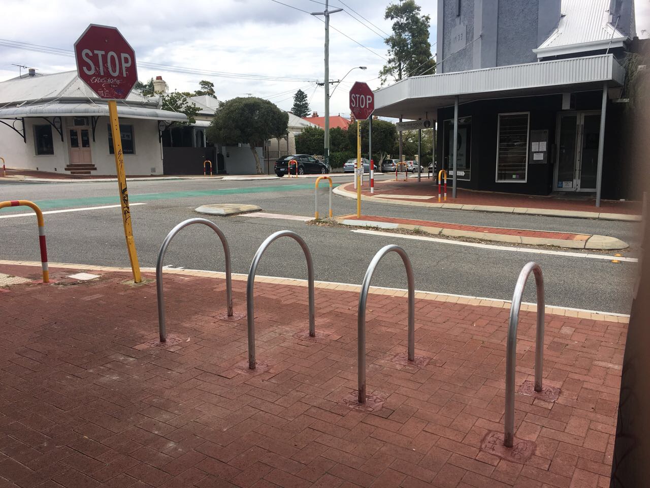 Bike racks on a brick sidewalk near a street intersection with stop signs. Tips for locking your bike to bike racks for security.