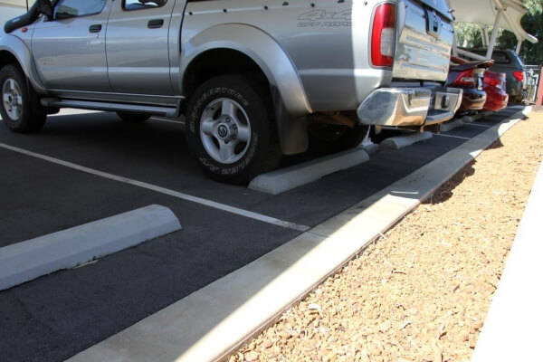 Cars parked in a row using concrete wheel stops. Choose the right wheel stops for parking safety and vehicle control.