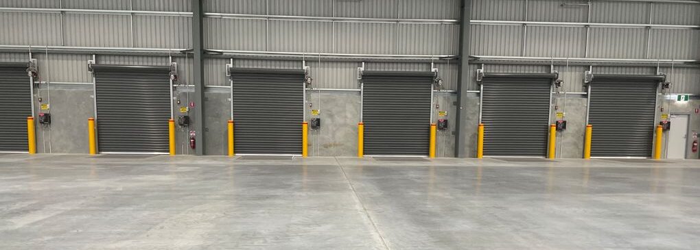 Warehouse interior with multiple roller doors and Dugite Safety Yellow 165mm bollards protecting each door.