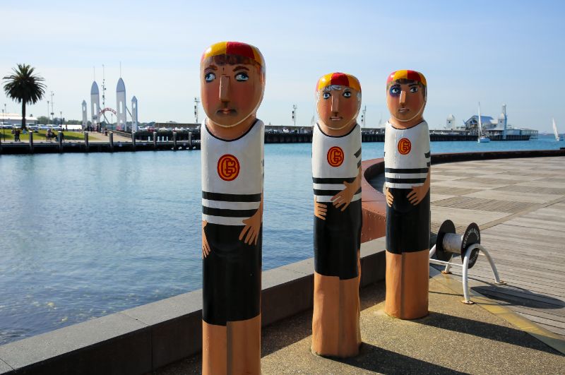 Decorative bollards protect facilities. Three painted bollards depicting lifeguards stand by a harbor on a sunny day.