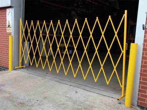Yellow expandable safety barrier gate in a warehouse. Expandable barriers improve visibility and safety in industrial settings.