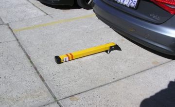 Fold down parking bollard in lowered position. Yellow post is on the ground by a parked car, increasing parking safety.