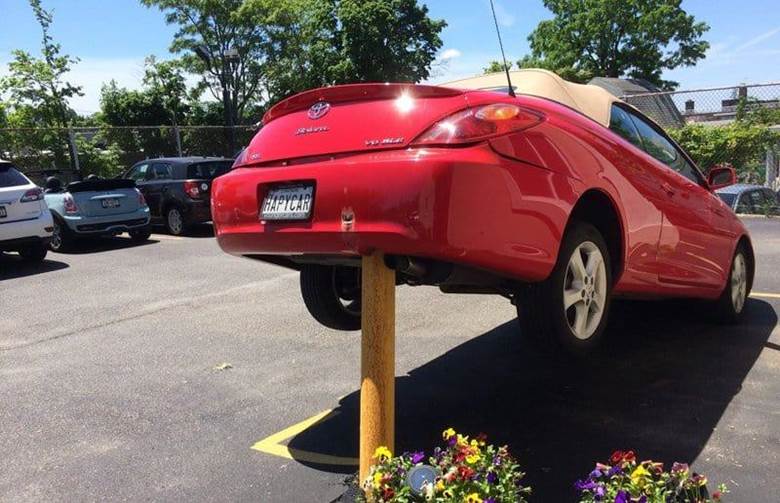 Red convertible impaled on bollard in car park. Preventable car accidents happen; this one features a car with the license plate HAPYCAR.