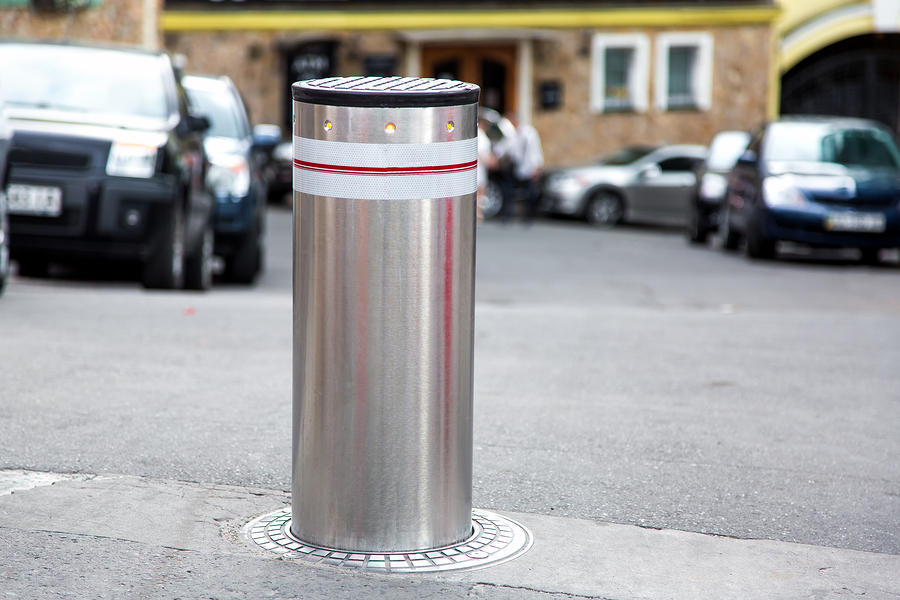 Upright semi-automatic bollard. Silver metal post with reflective stripes on a city street. DIY security solution for traffic control.