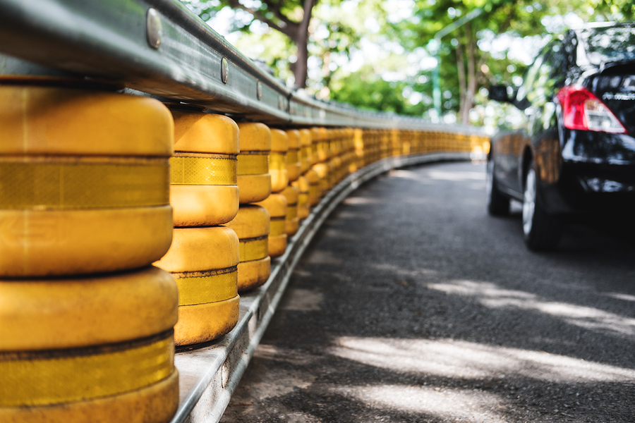 Road Railing Safety Barrier Why Our Roads Need Safety Barriers 1 Road safety barriers with yellow drums line a curved road, protecting vehicles. A black car is partially visible on the road.