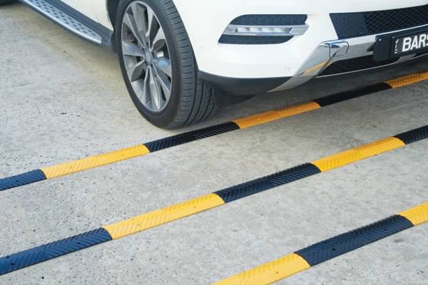 Car approaching rumble strips, a traffic calming safety feature. Yellow and black strips on the road. How do rumble strips work to alert drivers?