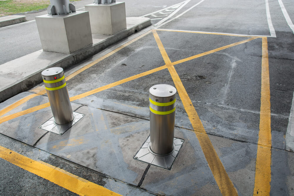 Silver security bollards with yellow bands on a concrete surface with yellow lines, used for choosing bollard locations.