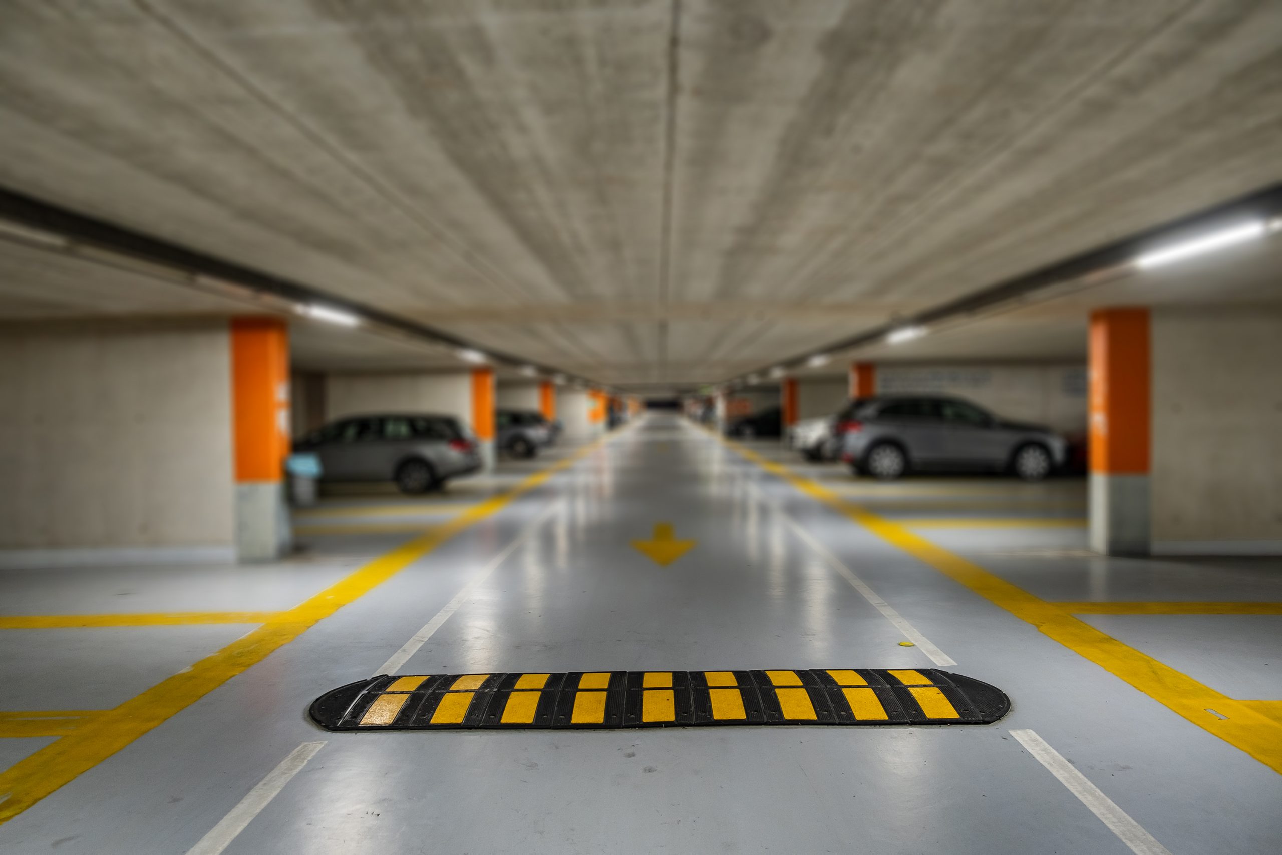 Underground car park safety feature: speed bump with yellow stripes. Cars parked in the background. Improving car park safety with speed control.