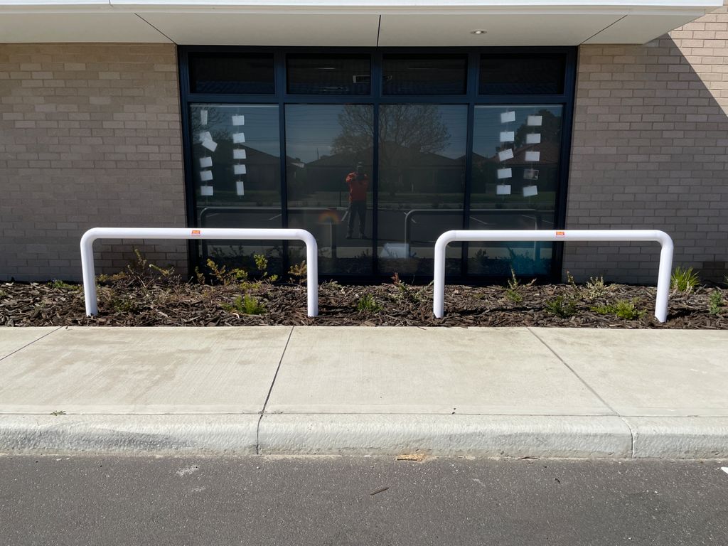 U Bars installed Dugite Barrier Rail 2000mm White 12 Two white Dugite Barrier Rails 2000mm protect a building's window from pedestrian traffic. The barrier rails are placed on a concrete sidewalk.