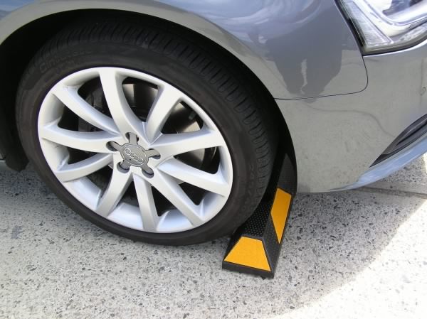 Car tire against a black and yellow parking wheel stop. The wheel stop is a safety measure in a parking area.