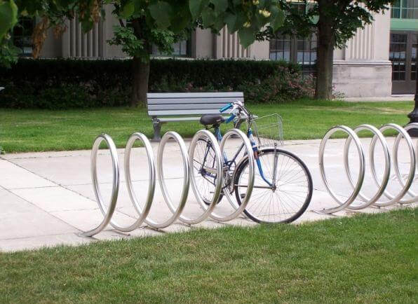 bike parking guidelines Perth Bike Parking Guidelines 1 Perth Bike Parking: A blue bicycle secured in a modern, circular metal bike rack on a sidewalk next to green grass and a bench.