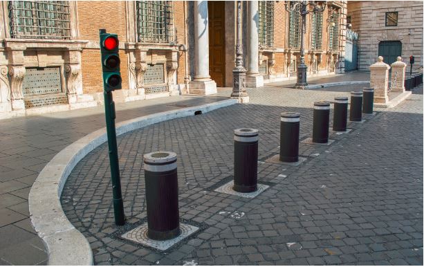 Row of black bollards, types of bollards, on a cobblestone street with a traffic light showing red, near an old building.