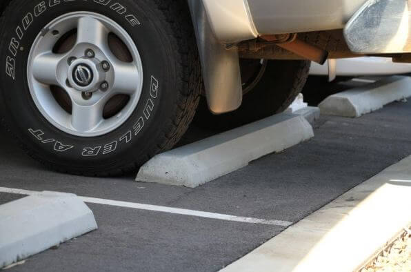 Car wheel against a concrete wheel stop in a car park. Gray concrete parking block prevents vehicle from pulling too far into the parking space.