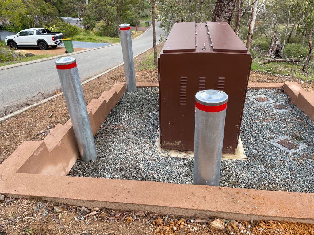 d219 with added red band Dugite 219mm x 2000mm In Ground Bollard Galvanised 4.5mm Wall 3 Dugite 219mm Galvanised In Ground Bollard. Silver bollards with red tops surround a brown electrical box. Gravel ground cover and concrete border.