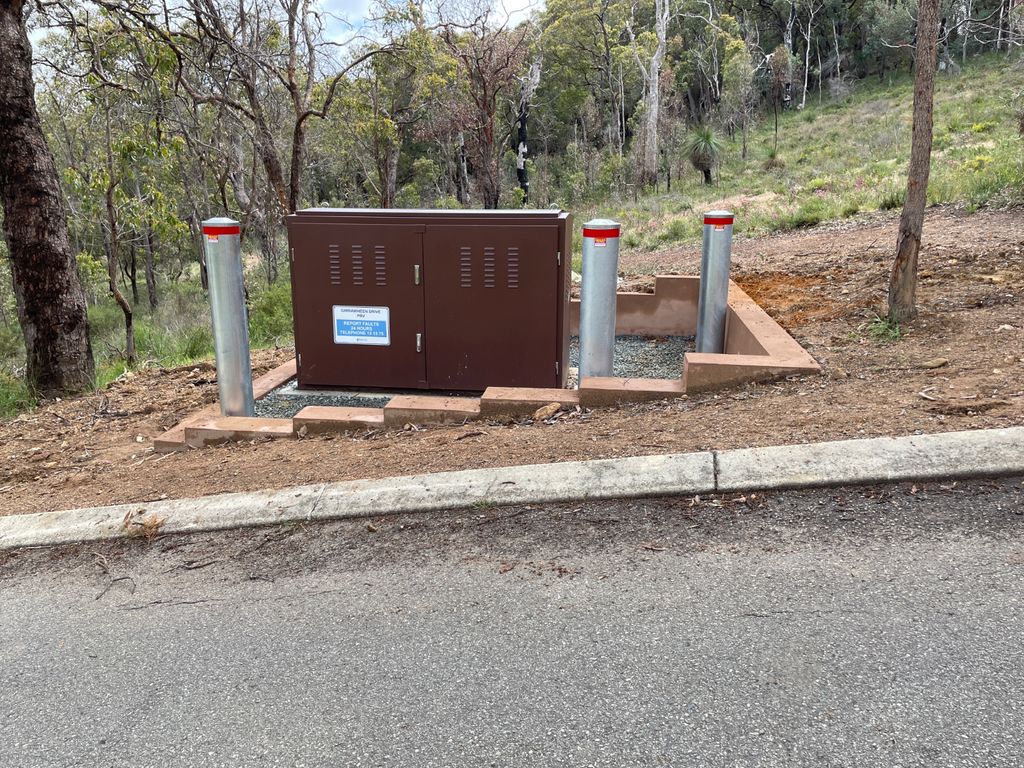 d219 Dugite 219mm x 2000mm In Ground Bollard Galvanised 4.5mm Wall 2 Dugite 219mm Galvanised In Ground Bollard, 2000mm height, 4.5mm wall thickness, protects brown electrical box near a road in a wooded area.
