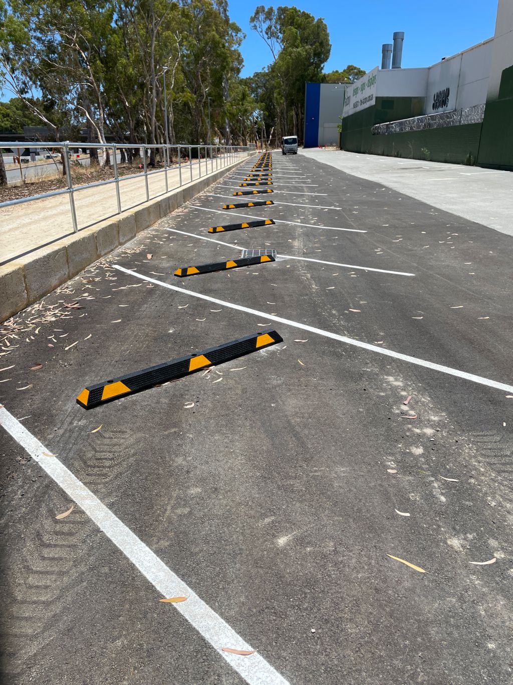 image Dugite Rubber Wheel Stop 1650mm x 95mm 2 Dugite 1650mm rubber wheel stop in a parking lot. Black wheel stops with yellow reflectors are installed in each parking space for safety.
