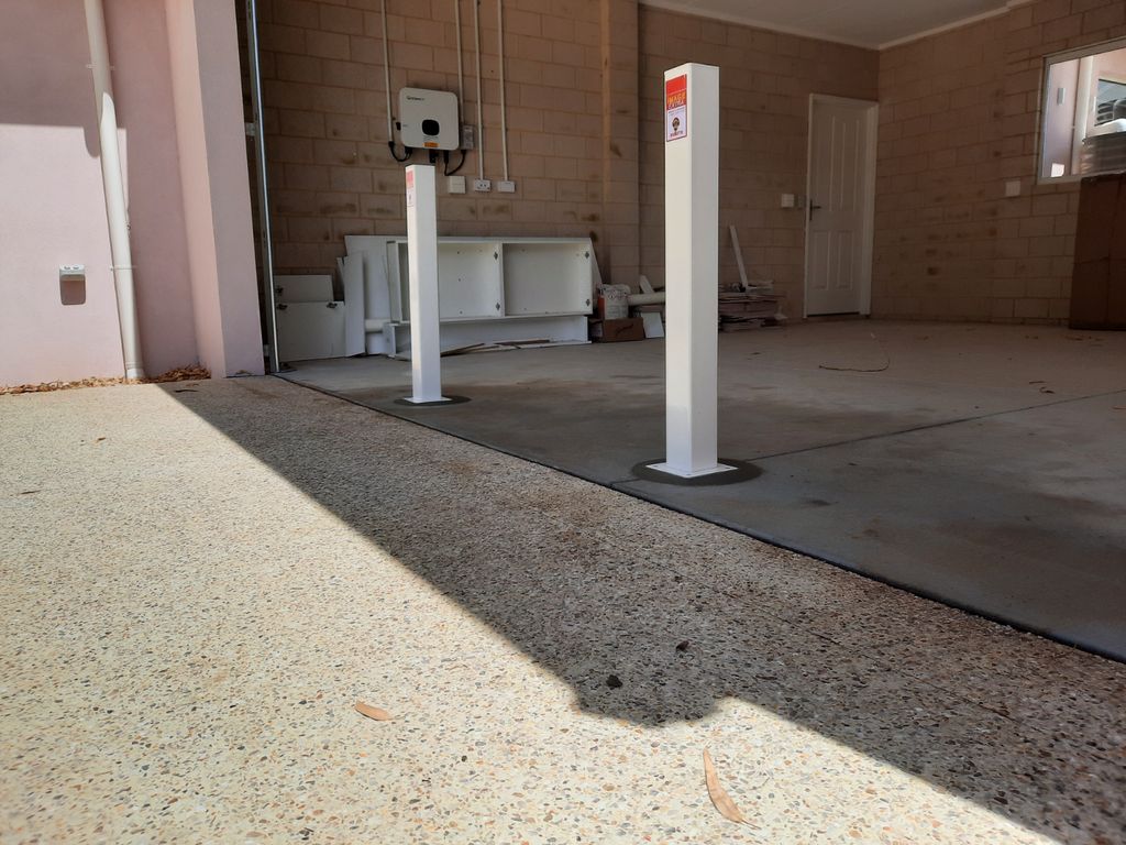 pic 1 Dugite Bronze 90mm x 900mm Retractable Bollard 4 Two Dugite Bronze 90mm x 900mm retractable bollards stand in an open garage. The bollards are white with warning labels on top, and the garage is unfinished.