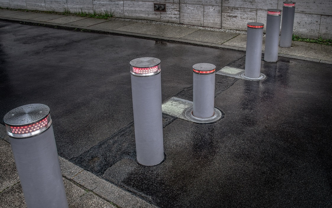 Vehicular Traffic Management: Retractable bollards with red lights line a wet city street. These posts aid in traffic control & security.