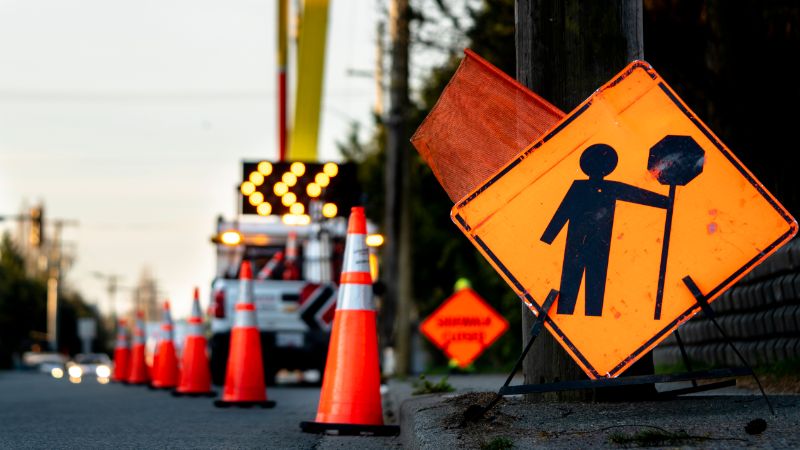 Road traffic management scene with orange cones, a truck with flashing arrows, and a road work sign. Caution, construction ahead.