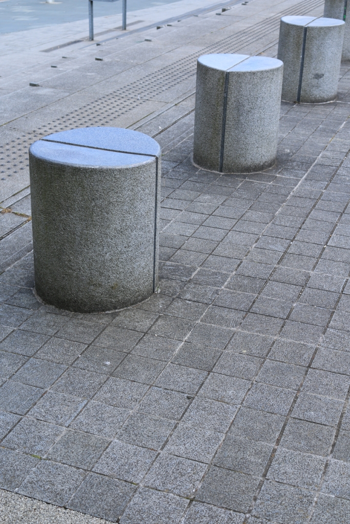 Gray round bollards on a gray tiled surface. Features to consider when choosing bollards include material, size, color, and design.