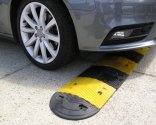 Car driving over black & yellow rubber speed hump. Installing speed humps helps control traffic speed and enhance safety in areas with pedestrian activity.
