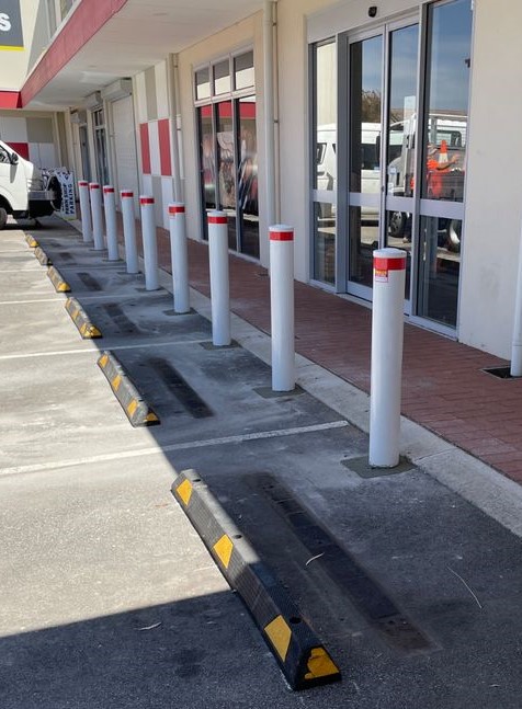 white inground bollards Dugite 140mm x 1500mm In Ground Bollard White 2 Dugite 140mm x 1500mm In Ground Bollard White. Row of white bollards with red tops outside a building. Parking bumpers on the ground.