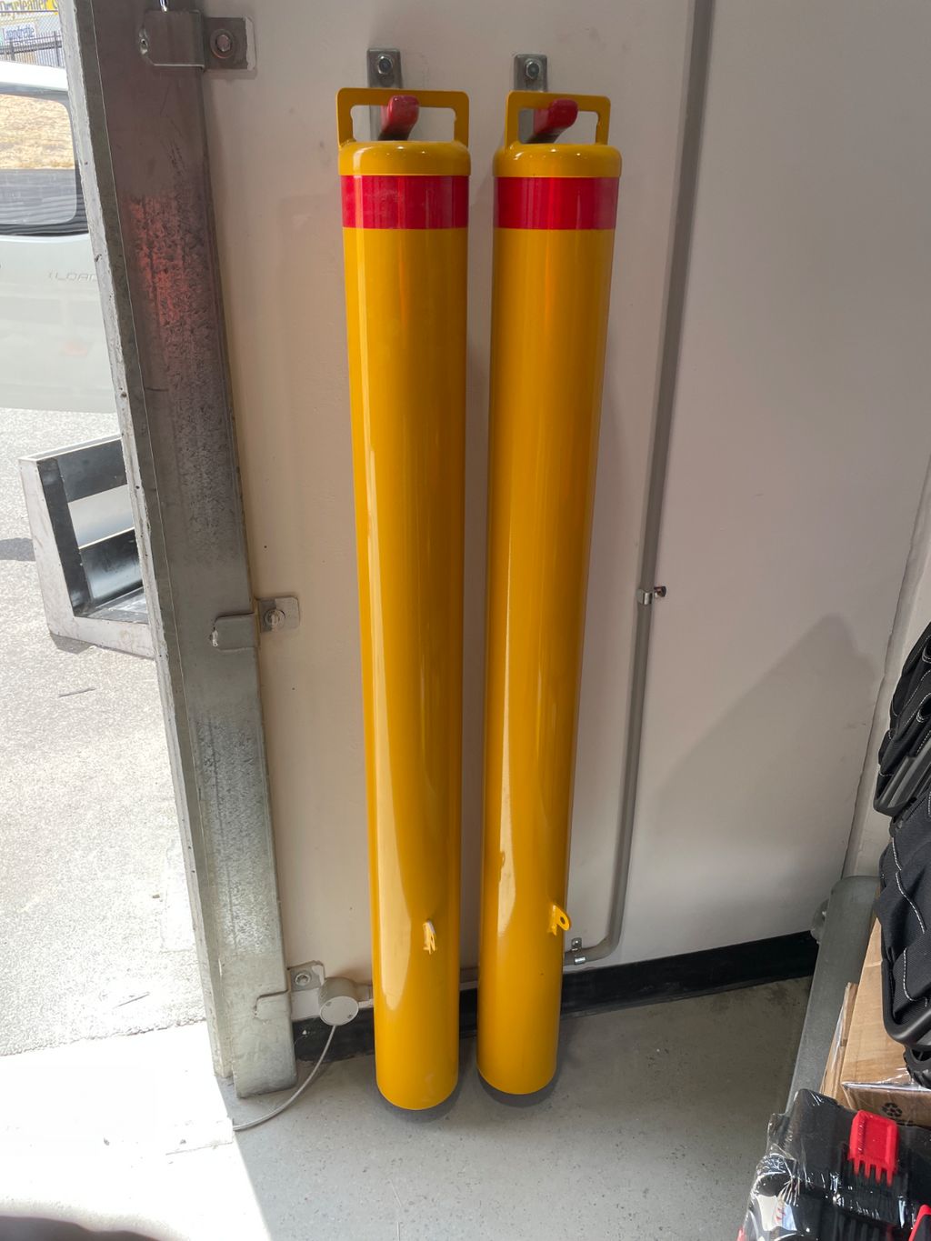 Bollard Hanging up Dugite 140mm x 1200mm Padlock Removable Bollard Round Safety Yellow 3 Two yellow bollards with red bands, mounted on a white wall. Safety equipment for traffic control and parking.