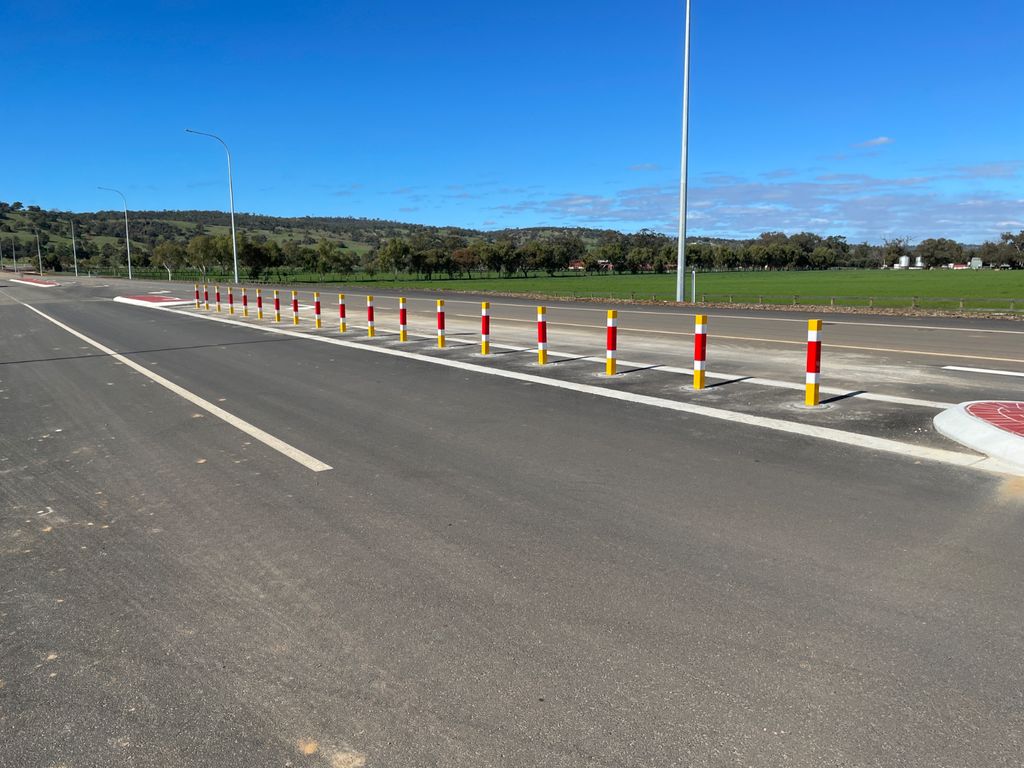 Retractable Bollards Removable vs. Retractable Bollards: Which One to Choose? 1 Roadway with removable bollards. Red, yellow, and white bollards line the street, offering a visual guide. Landscape with blue sky in the background.