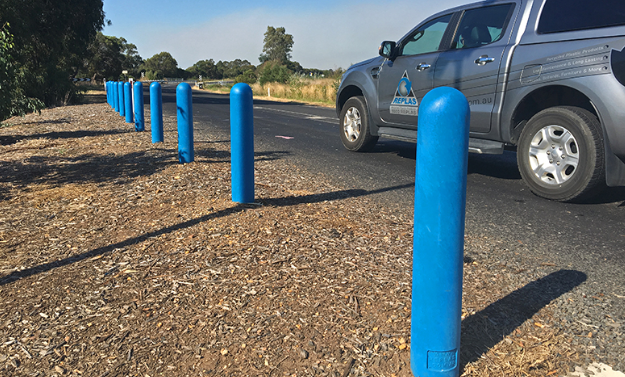blue bollards installed Non Conductive Bollard 150mm Round - Coloured Blue or Yellow 2 Blue 150mm round Non Conductive Bollard line a road. These bollards are designed for safety and visibility. A truck is parked nearby.